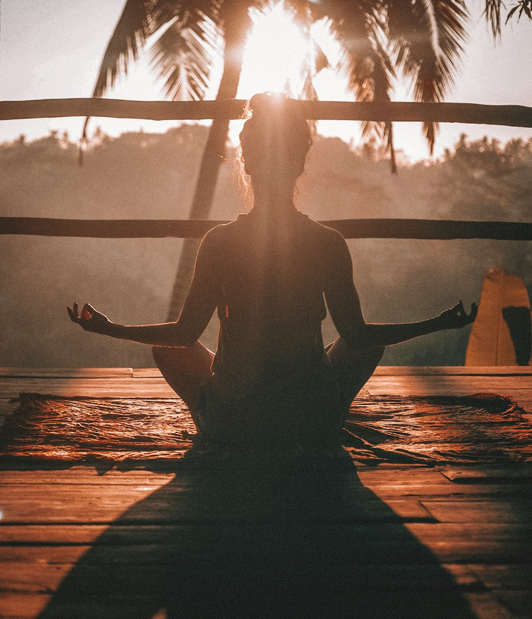 Person sitzt in Meditationspose, mit der Sonne im Hintergrund