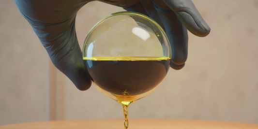 Hand in Laborhandschuh hält eine Glaskugel, aus der MCT-Öl fließt