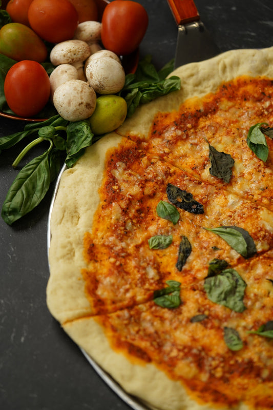 Pizza mit Oregano, Basilikum und frischen Zutaten daneben